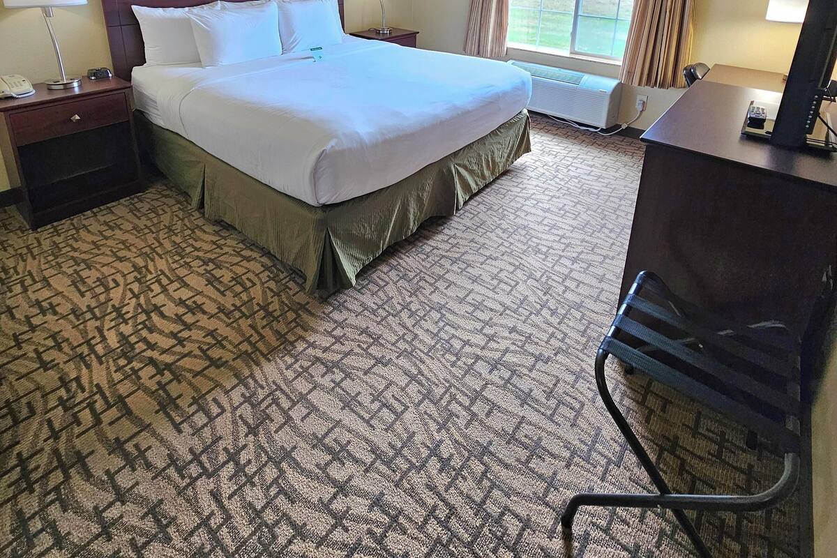 A hotel room with a large bed, two bedside tables with lamps, a desk with a computer, and a view of the outdoors through a window.