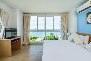 A hotel room with a large window, a bed, a TV on a wooden stand, and a view of the sea. - Best Bella Pattaya (Pattaya)