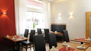 A hotel dining area with tables set for four, black chairs, and a large window with curtains.