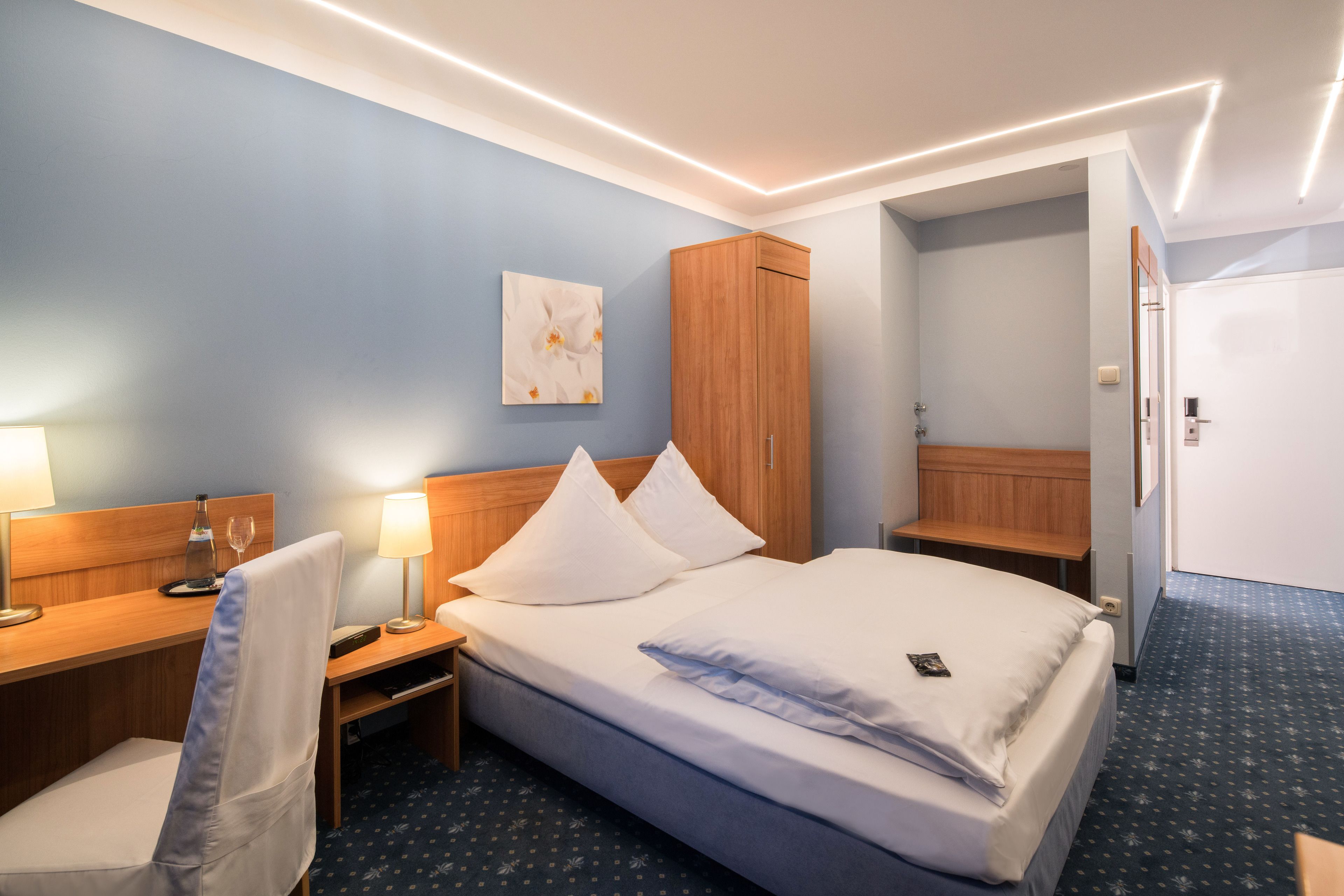 Habitación de hotel con cama, mesitas de noche, escritorio, silla, armario y puerta de baño.