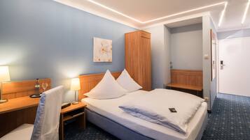 Habitación de hotel con cama, mesitas de noche, escritorio, silla, armario y puerta de baño.
