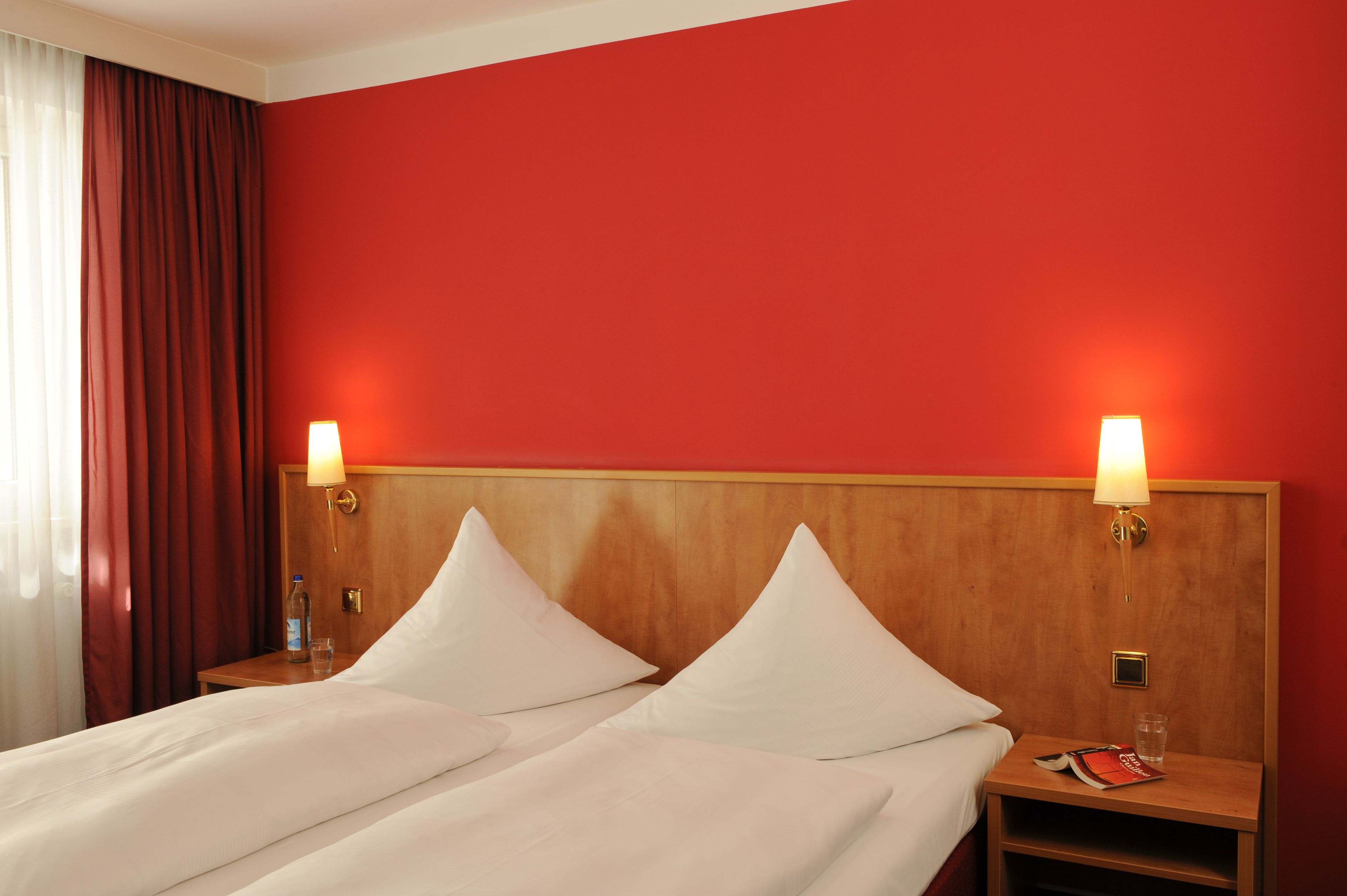 A hotel room with two beds, red walls, and bedside lamps.