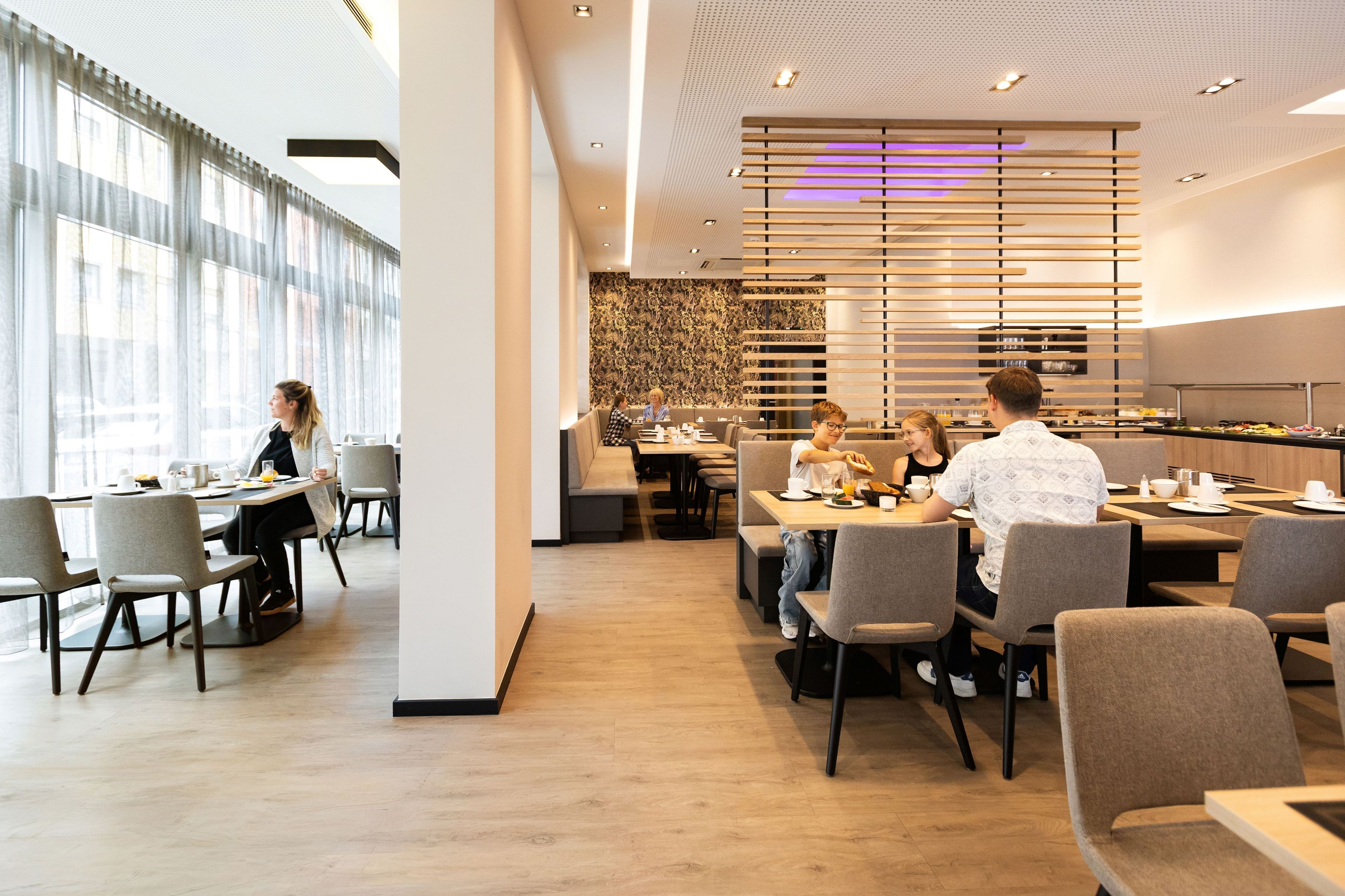 A modern dining area with multiple tables and chairs, a patterned wall, and a ceiling with recessed lighting.