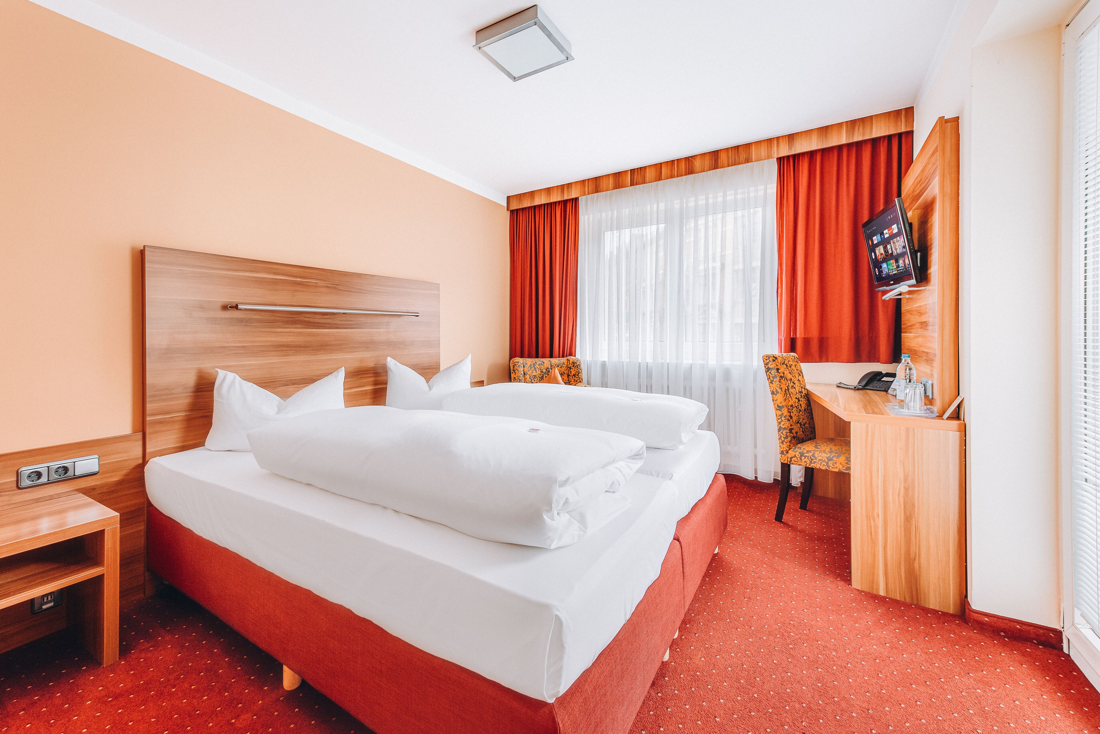 A hotel room with a bed, a desk, a chair, and a television.