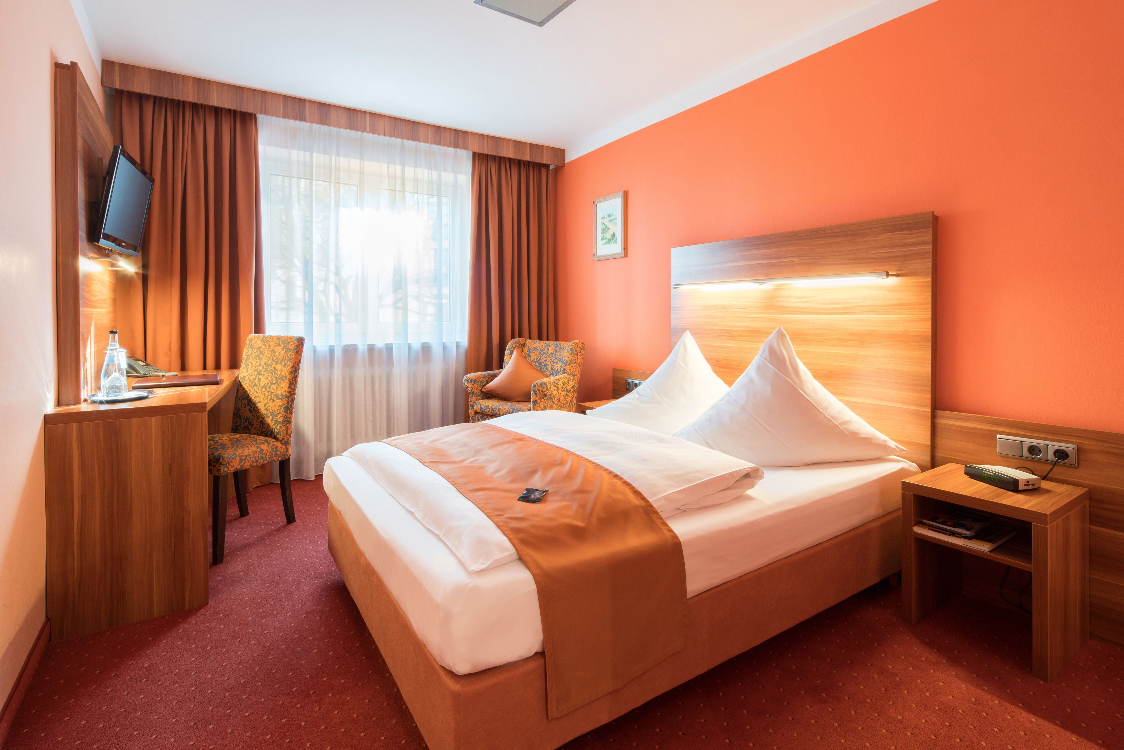 Habitación de hotel con cama, dos sillones, escritorio con televisor y mesita de noche con lámpara.