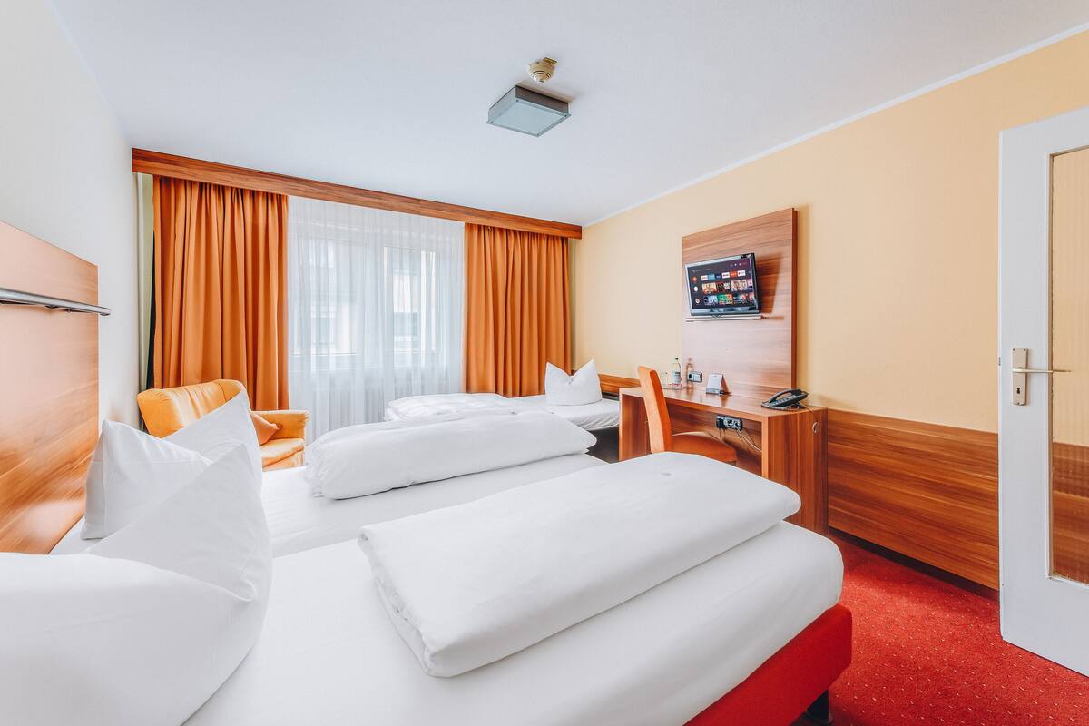 A hotel room with two beds, a desk, a chair, a television, and a door.