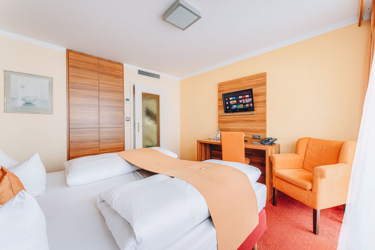 A hotel room with a bed, a desk, a chair, and a television on the wall.