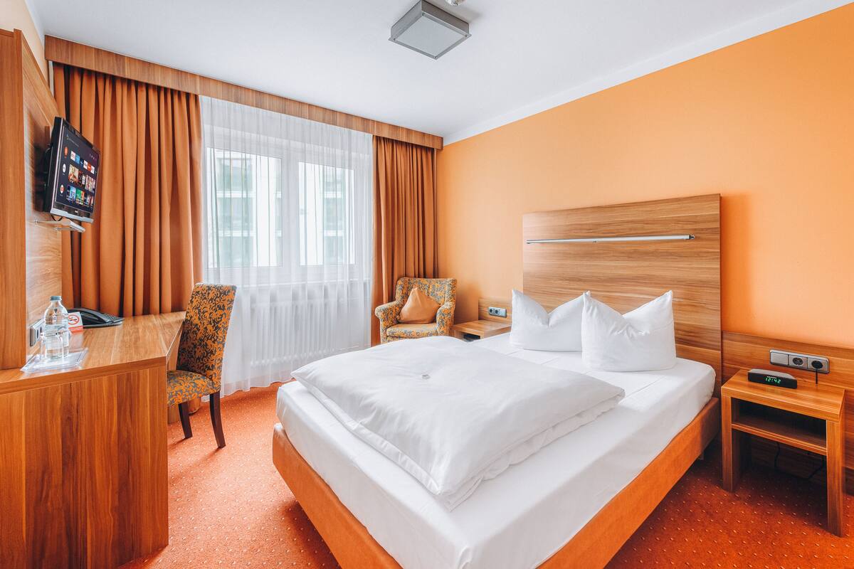 A hotel room with a large bed, a desk, a chair, and a television.