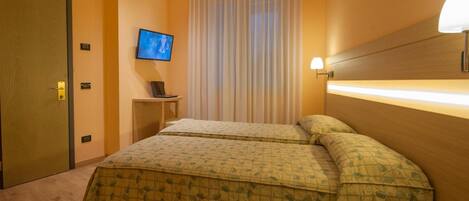 A hotel room with two beds, a television on the wall, a bedside table with a phone, and a curtain.
