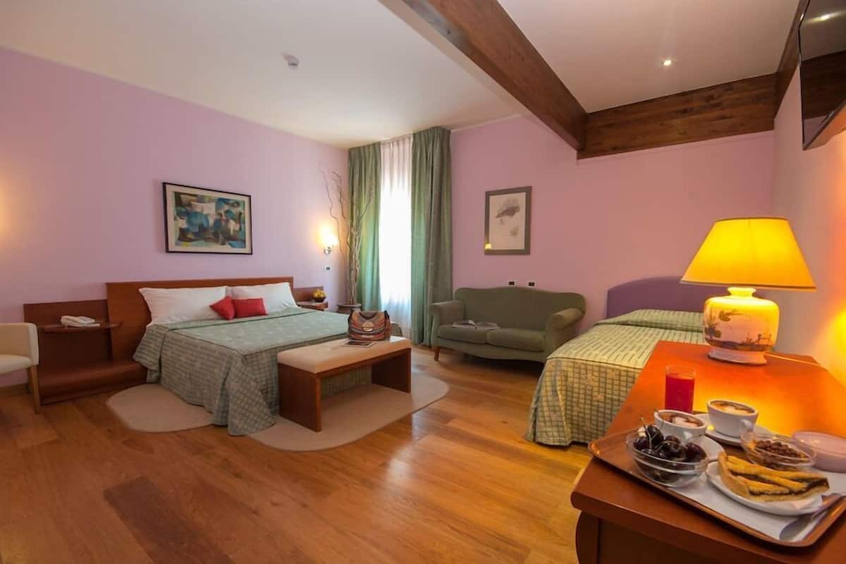 A room with a bed, a sofa, a small table with a lamp, and a tray with food.