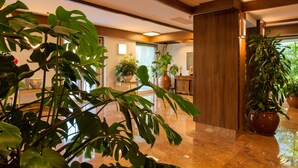 Un vestíbulo con grandes plantas en macetas, un mostrador de recepción de madera y un piso de mármol pulido.