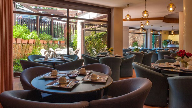 Un restaurante con mesas y sillas redondas, ventanas amplias y lámparas colgantes.