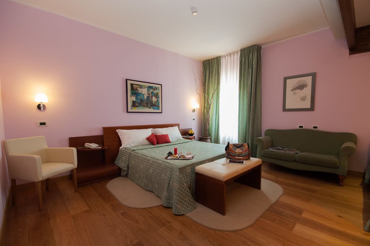 Un dormitorio con cama, mesita de noche, lámpara, silla y sofá.