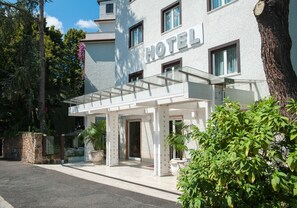 A modern hotel with a glass entrance, a sign indicating it's a hotel, and a well-maintained garden area. - Hotel La Pergola (Rome)