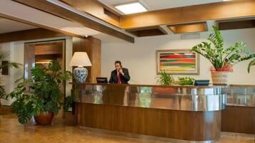 A reception desk with a receptionist, a large vase, and potted plants.
