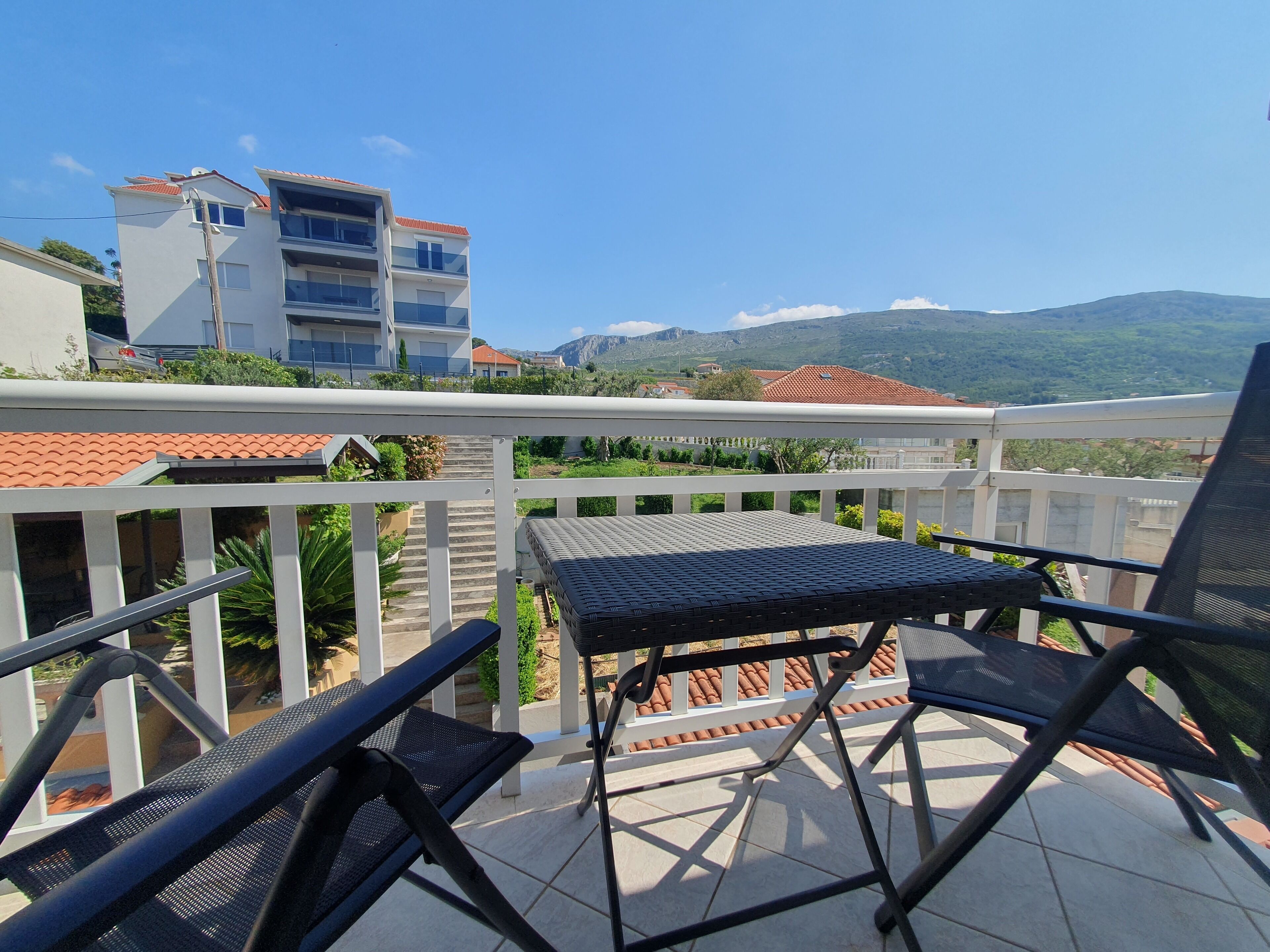 A balcony with a table and chairs, overlooking a residential area with buildings and a mountain in the distance.