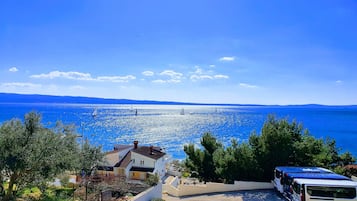 Vista costera con mar azul turquesa, algunas embarcaciones de vela y una fila de autobuses estacionados.