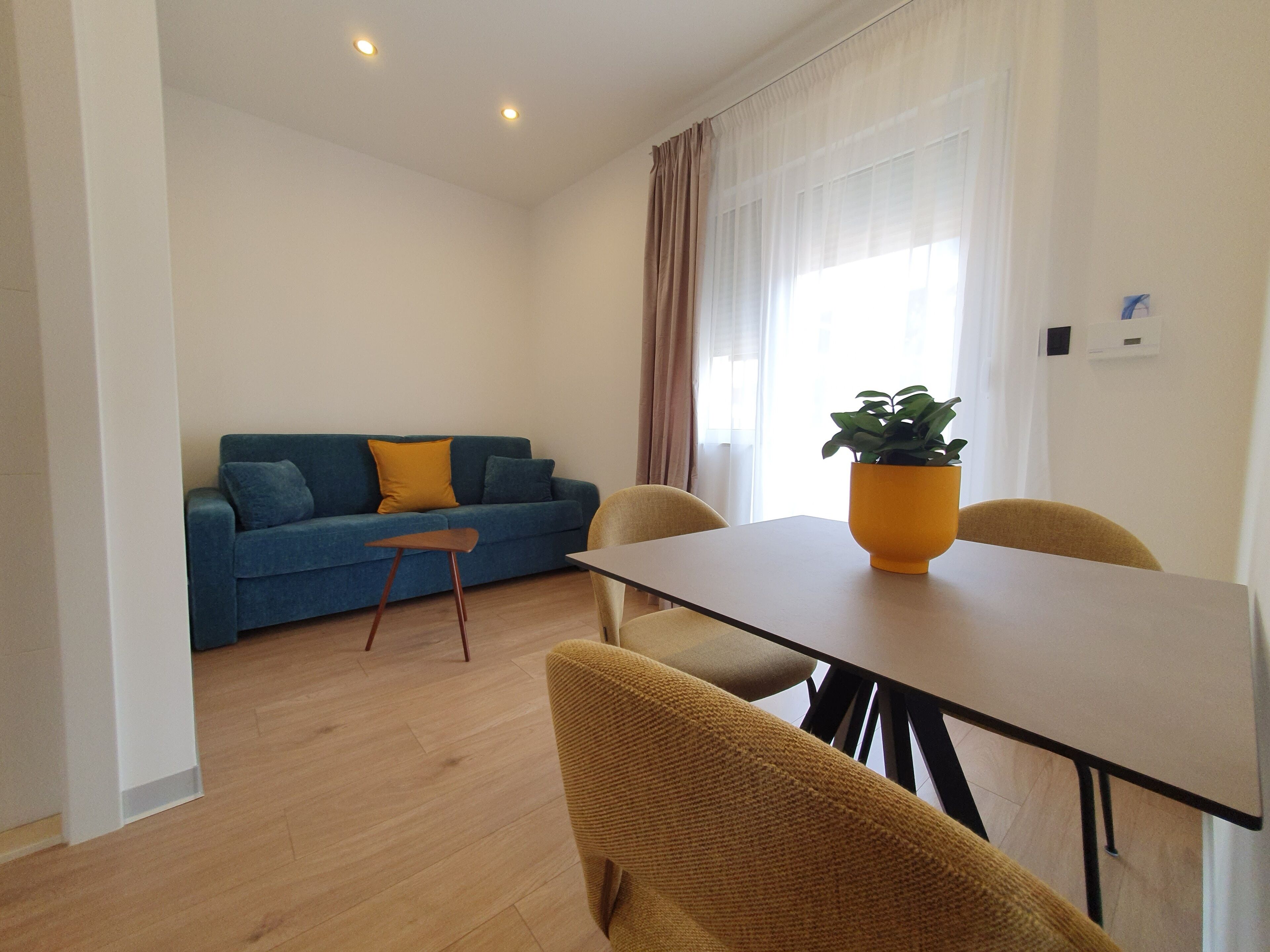 A modern living room with a blue sofa, a small wooden table, and yellow chairs.