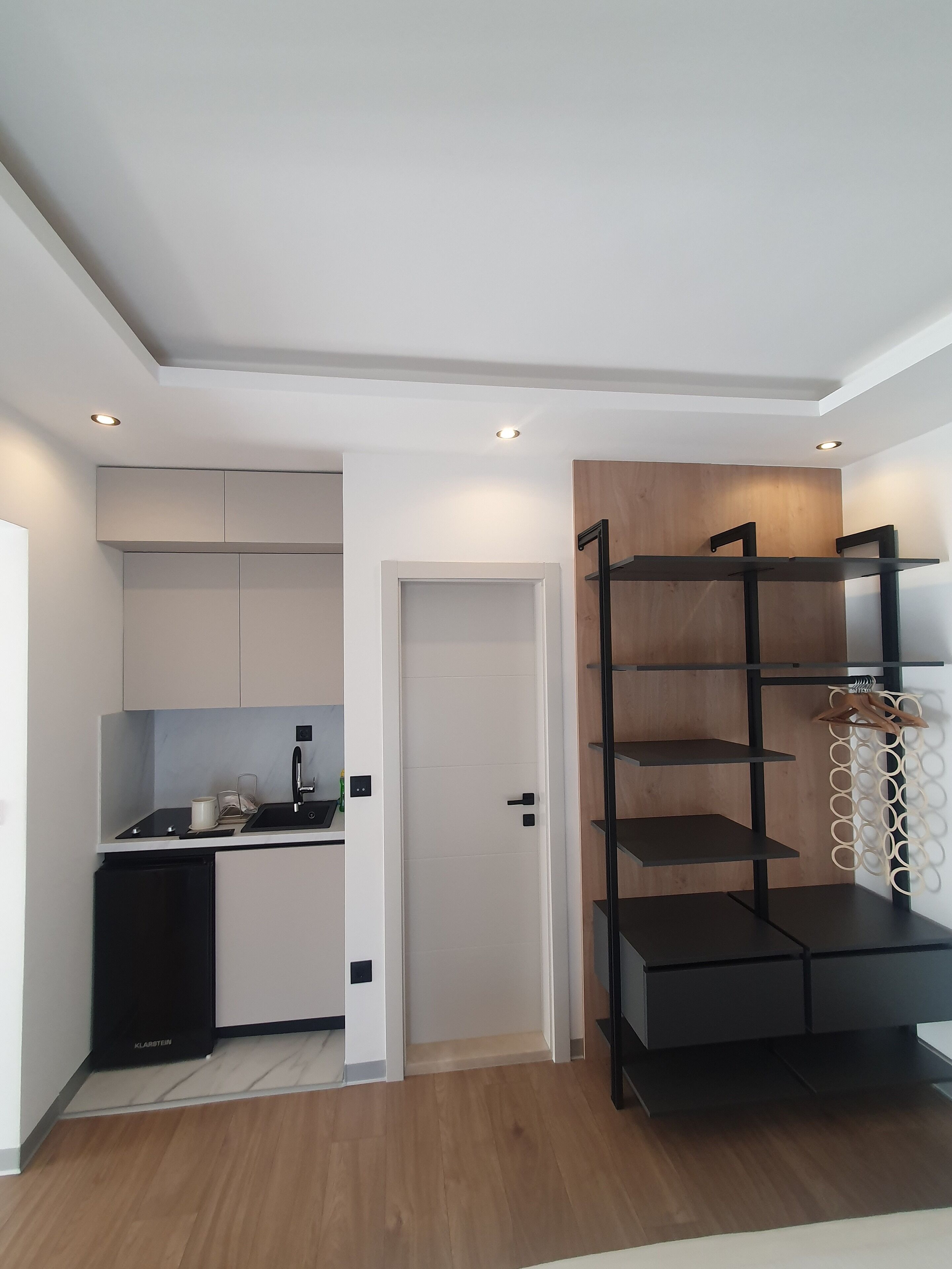 A modern kitchen with white cabinets, a black dishwasher, and a wooden door.