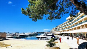 Un puerto deportivo con yates amarrados, un hotel moderno con balcones y un cielo azul despejado.