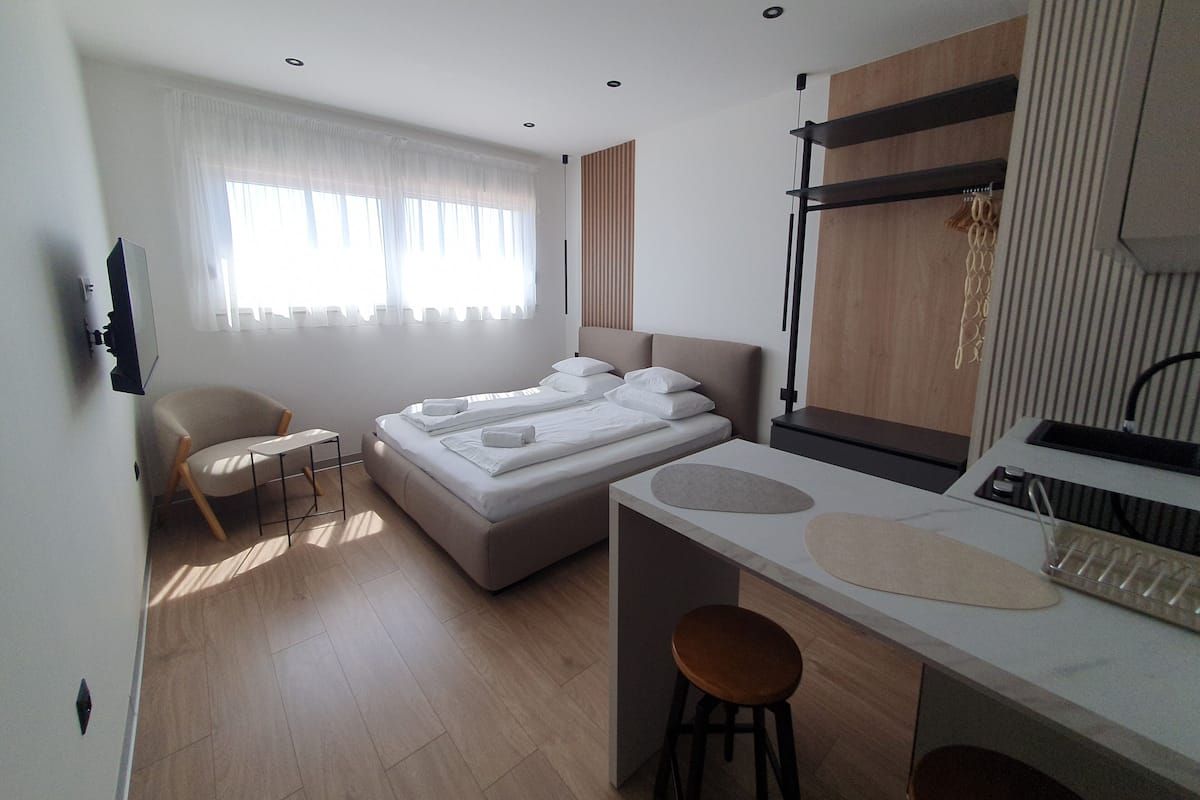 Una camera d'albergo moderna con un letto, una sedia, un tavolino e un angolo cottura.