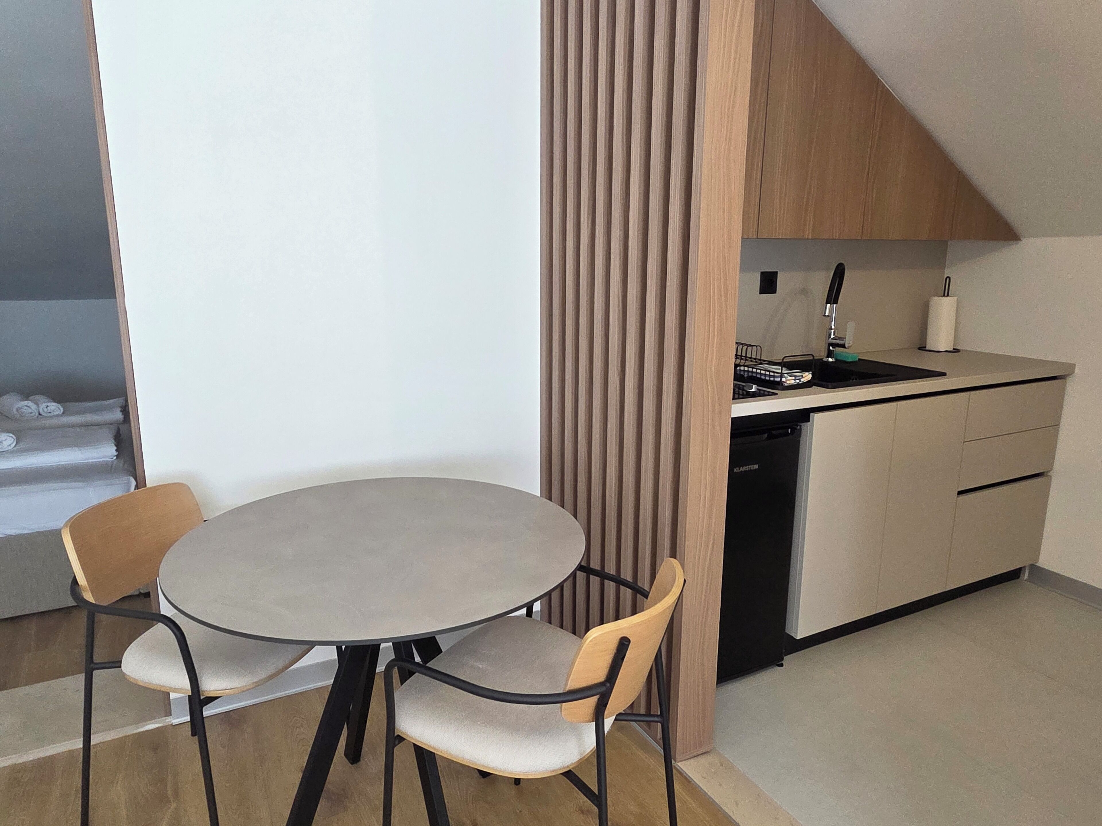 A compact kitchen with a round table and two chairs, a dishwasher, and a wooden cabinet.