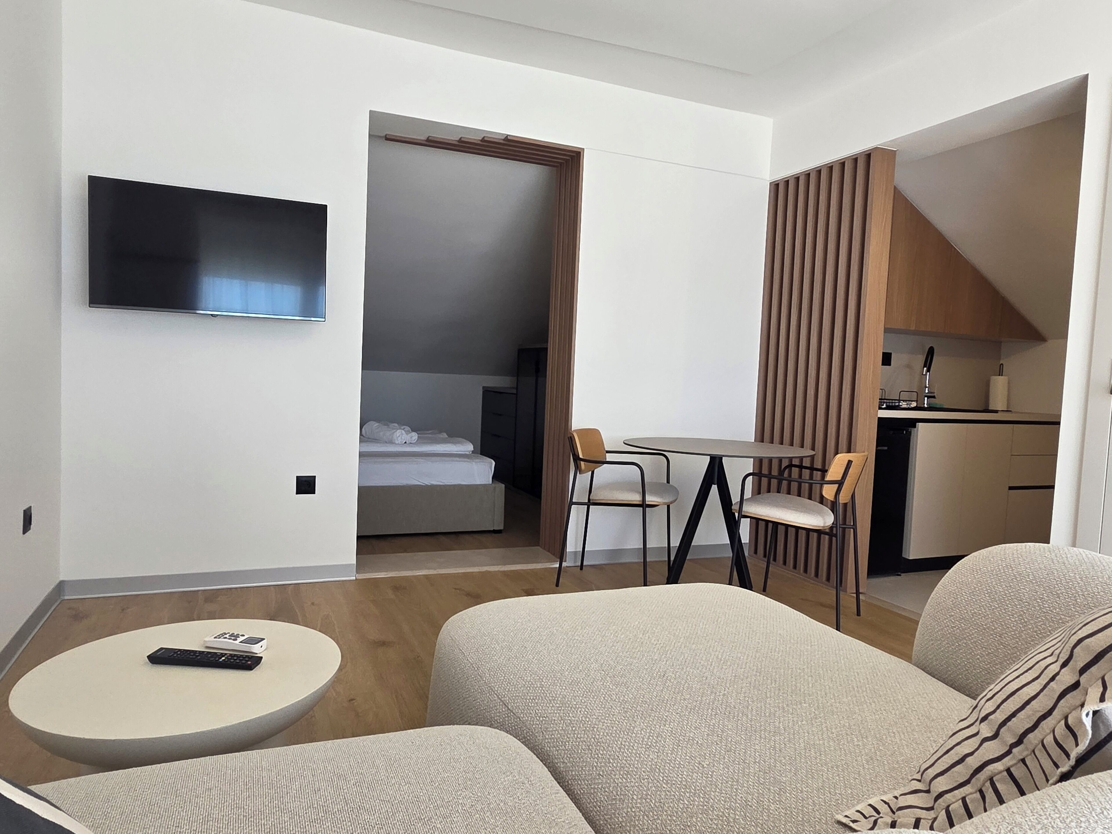 Habitación de hotel con televisión, cama, zona de comedor con sillas, una mesita pequeña y una kitchenette.