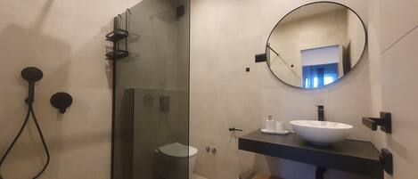 A modern bathroom with a glass shower enclosure, a round mirror, and a white sink.