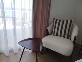 Una habitación con vistas a través de un ventanal grande, una silla y un sofá con cojines a rayas.