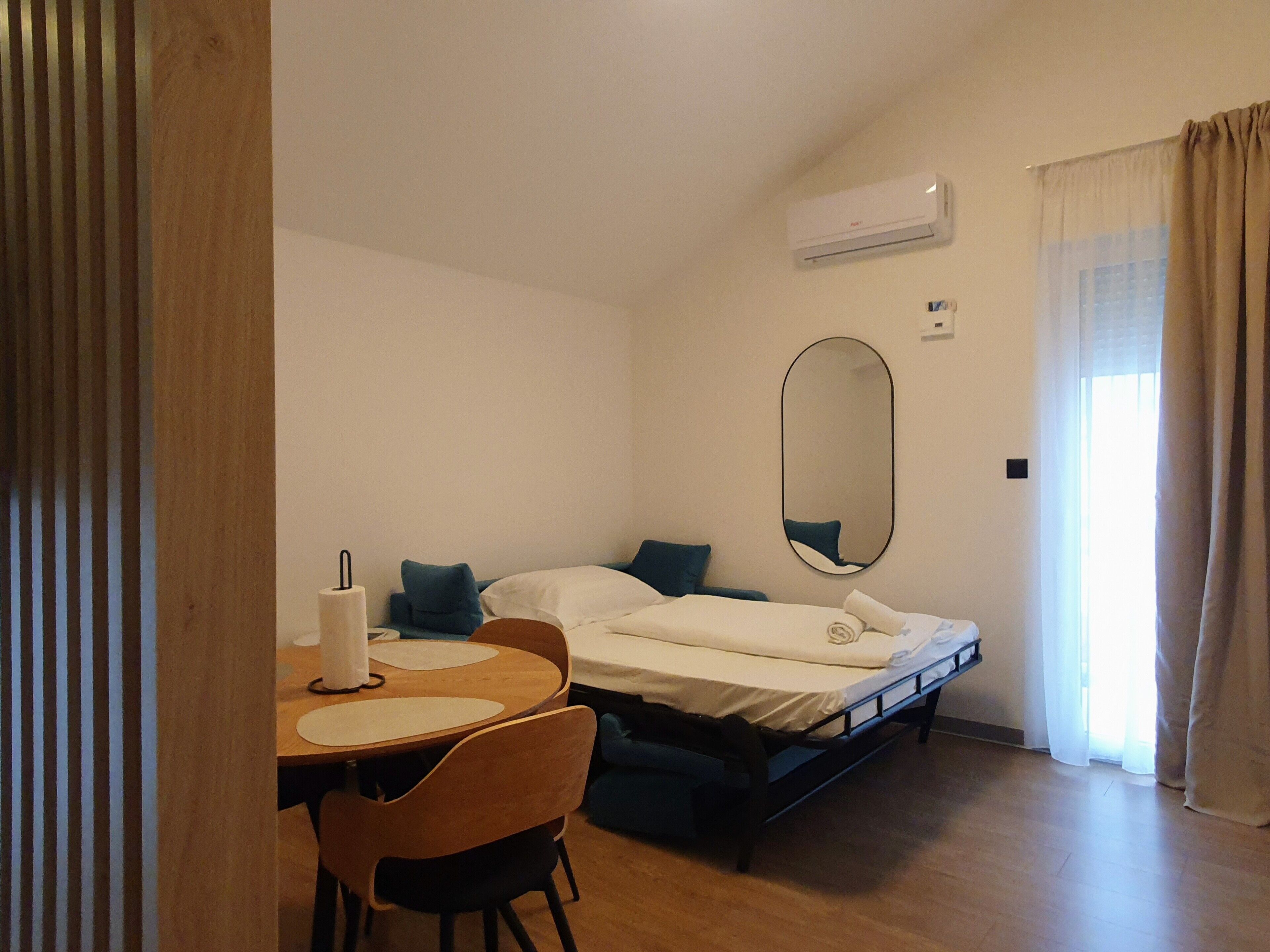 Een hotelkamer met een bed, een ronde tafel met stoelen, een spiegel en een airconditioning.
