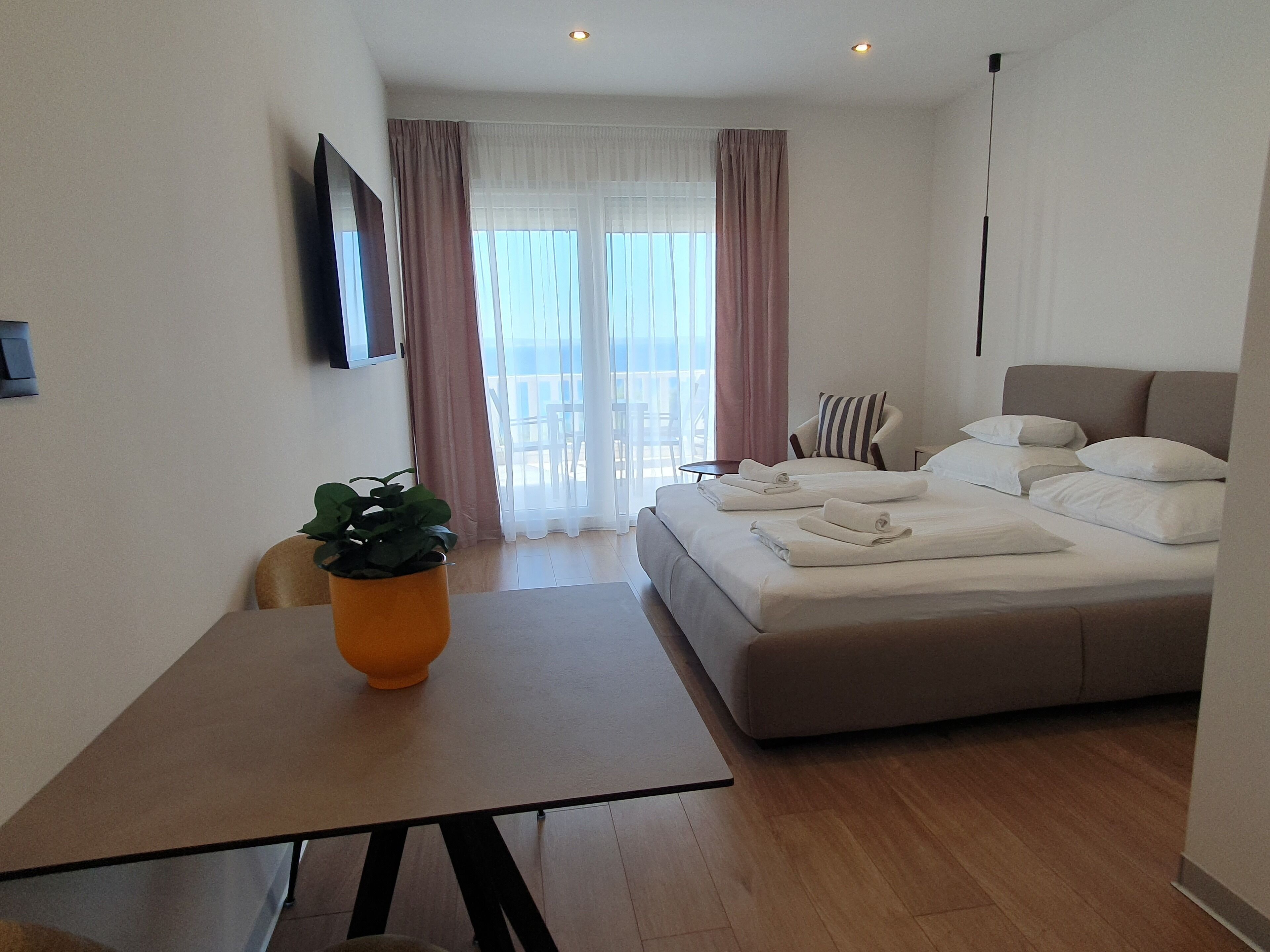 A modern hotel room with a bed, a table with a plant, and a balcony view.