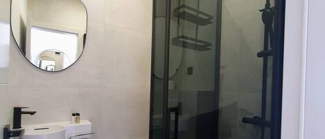 A modern bathroom with a glass-enclosed shower, a white sink with a mirror above it, and a toilet.
