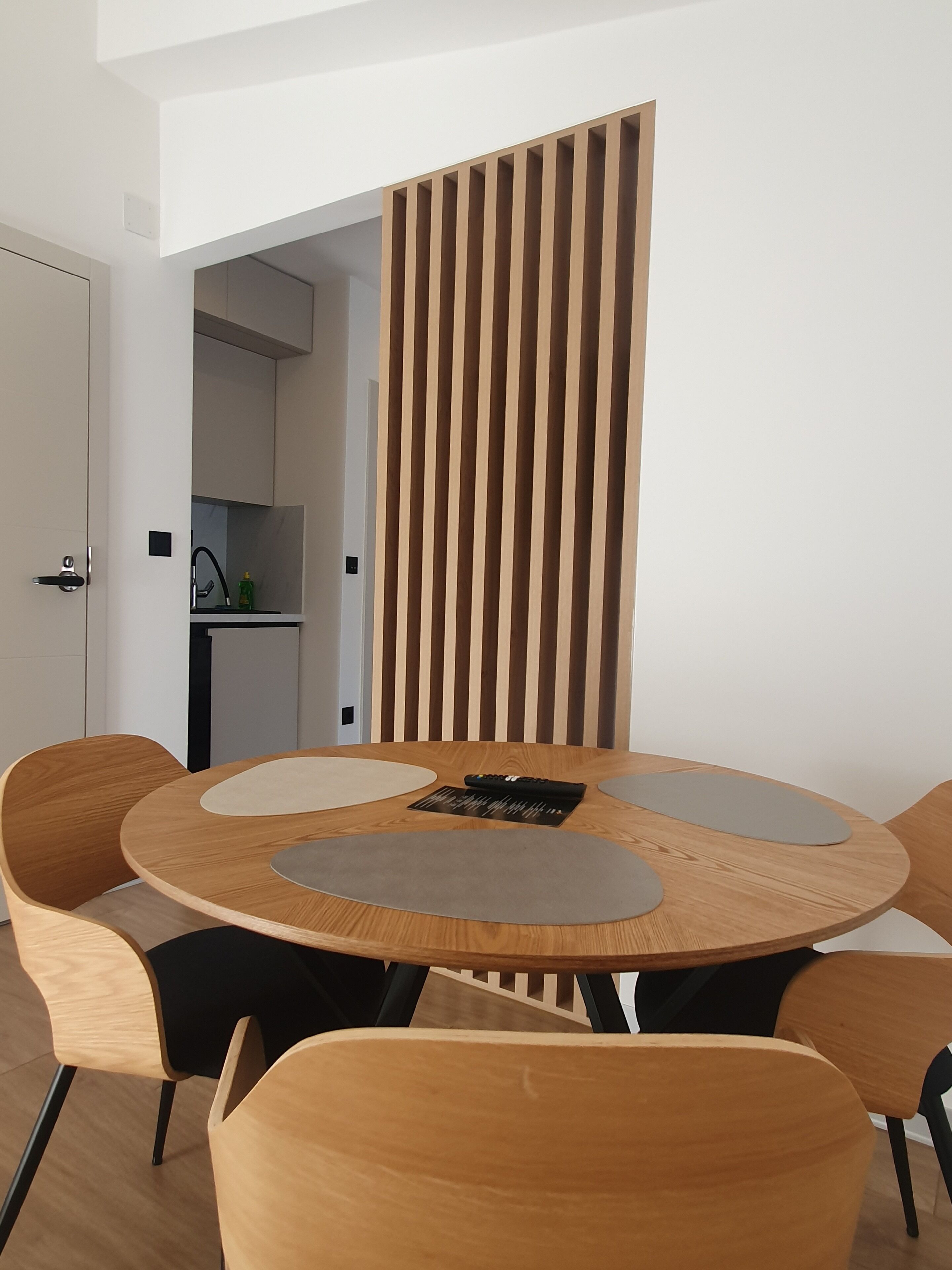 A modern dining area with a round wooden table, four matching chairs, and a vertical wooden slat partition.