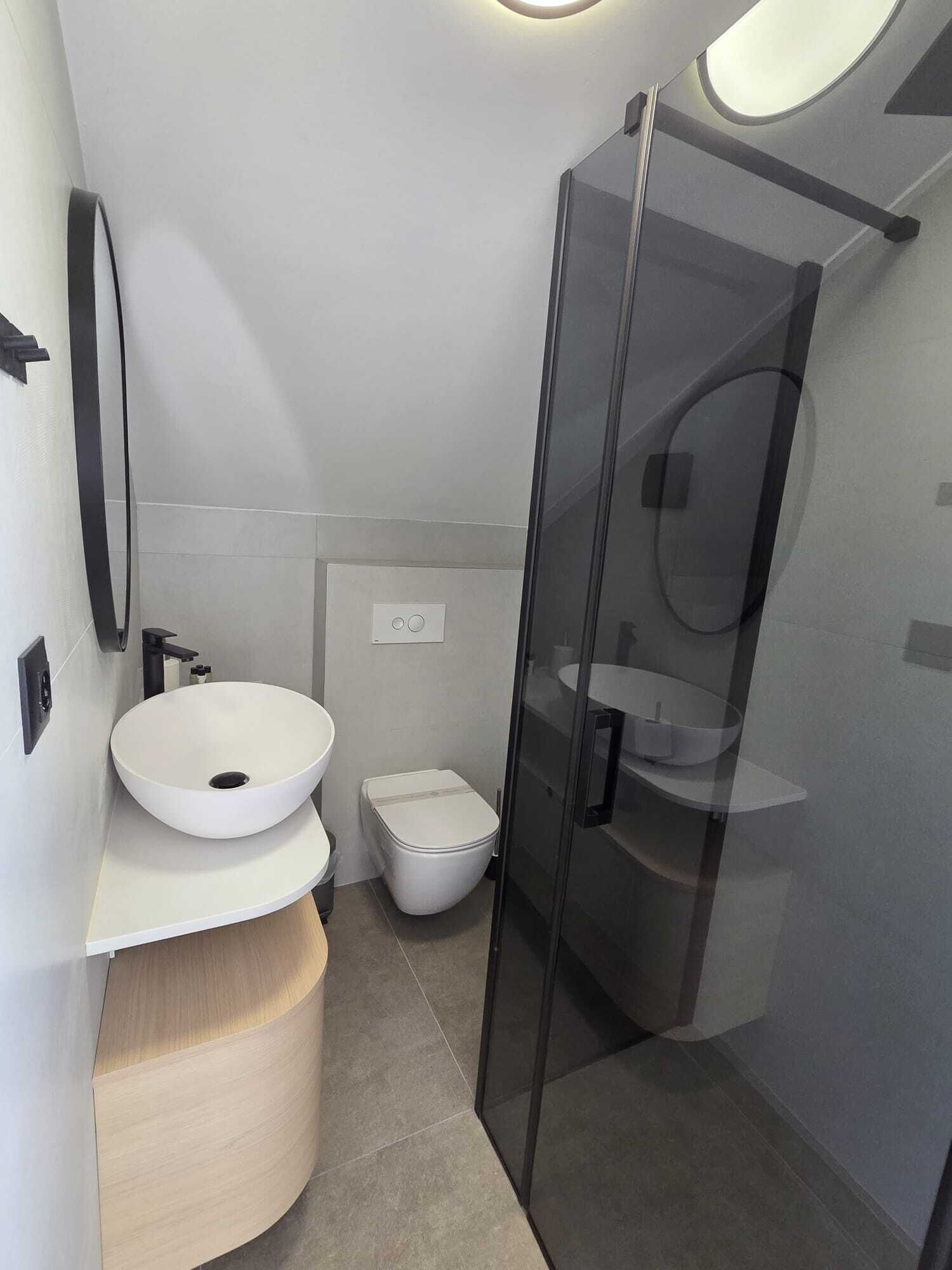 Et moderne badeværelse med en hvid vask, toilet og en brusekabine med glasvægge.