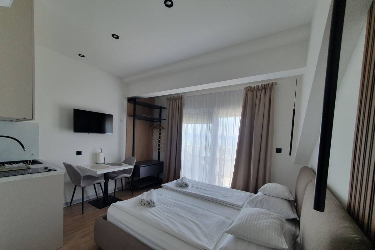 Una moderna camera d'albergo con un letto, una scrivania, una sedia, una TV e una finestra con tende.