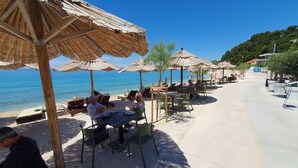 Un café frente a la playa con mesas al aire libre y sombrillas, con vistas al mar.