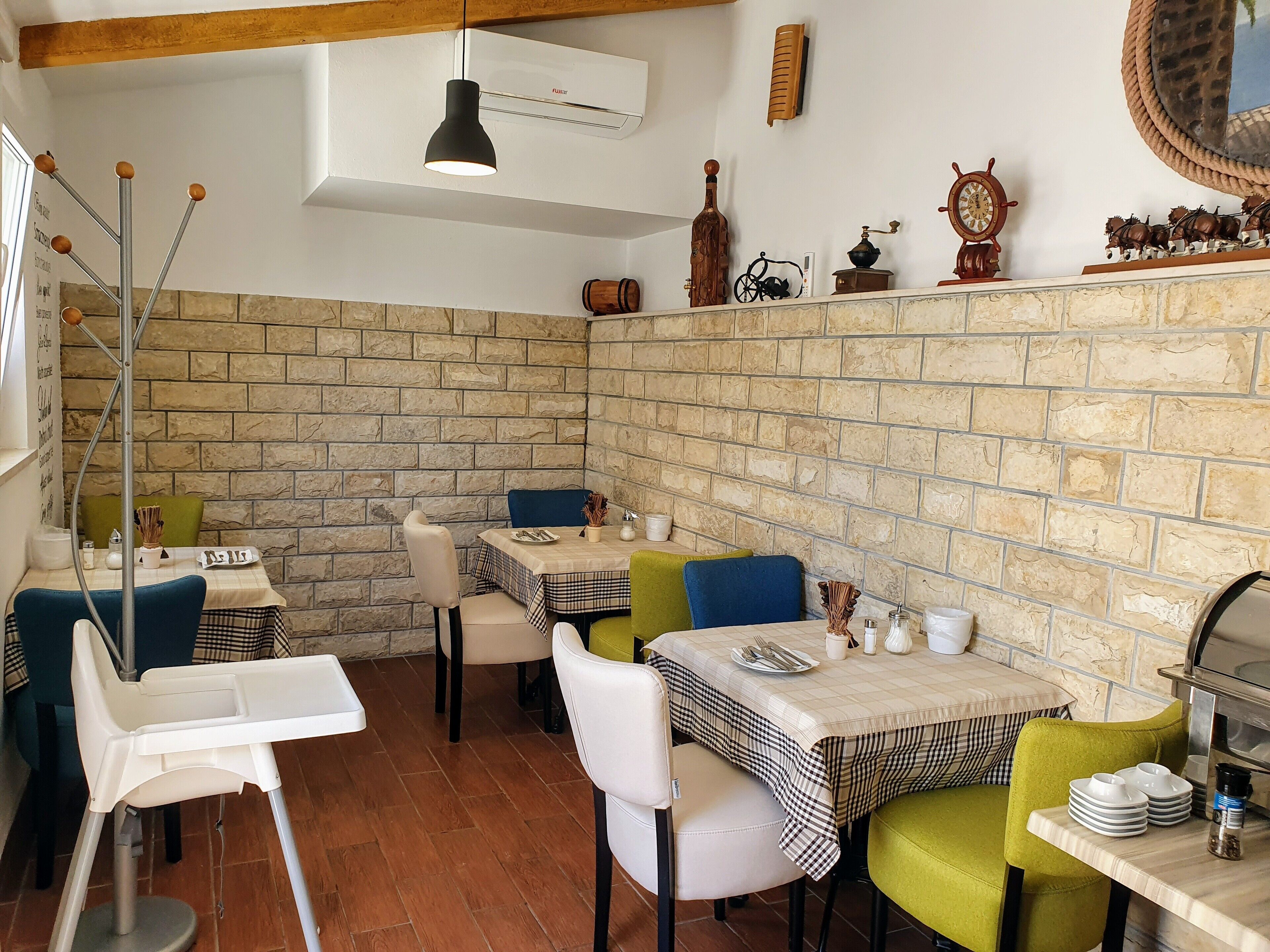 L’intérieur d’un restaurant présente des murs en pierre, de nombreuses tables recouvertes de nappes à carreaux et divers objets décoratifs accrochés aux murs.