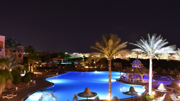 Ein Nachtblick auf einen Resort-Poolbereich mit großem Pool, Palmen und einer Bar.