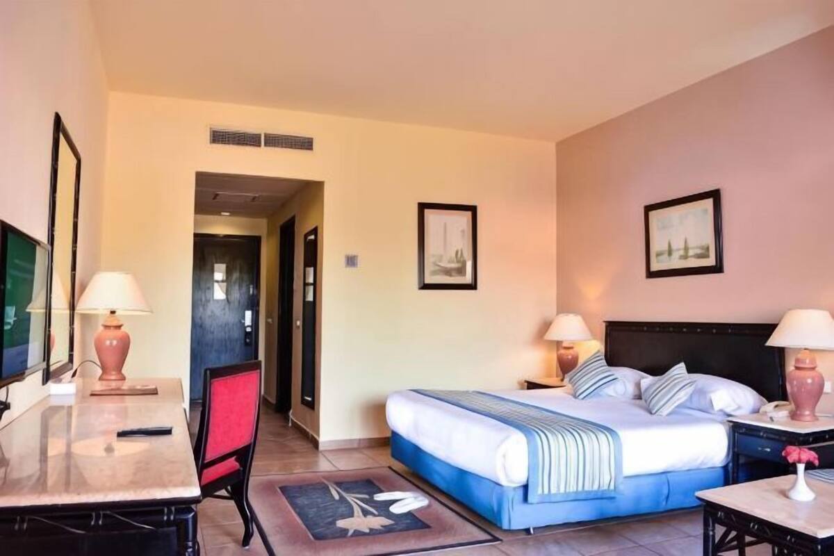Une chambre d’hôtel comprenant un lit, deux tables de chevet, un bureau, une chaise, un téléviseur et des œuvres d’art accrochées aux murs.