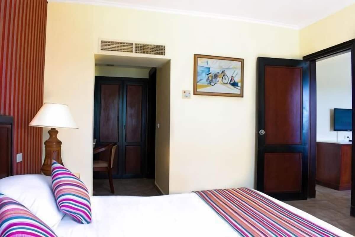 Une chambre d’hôtel avec un lit, une chaise, une lampe, un tableau et une porte.