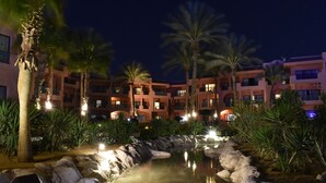 Ein Hotel nachts, bestehend aus mehreren Gebäuden, mit Palmen und einem Wasserspiel.