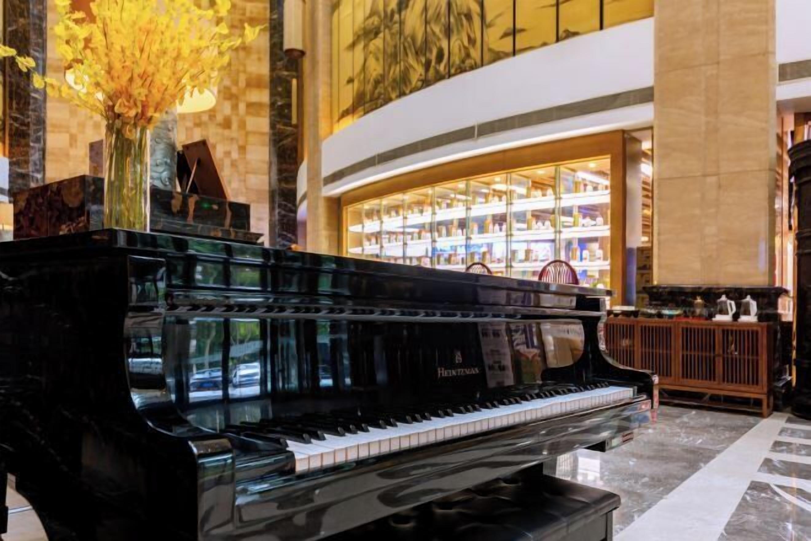A grand piano in a spacious lobby with a large, well-lit bookcase in the background.