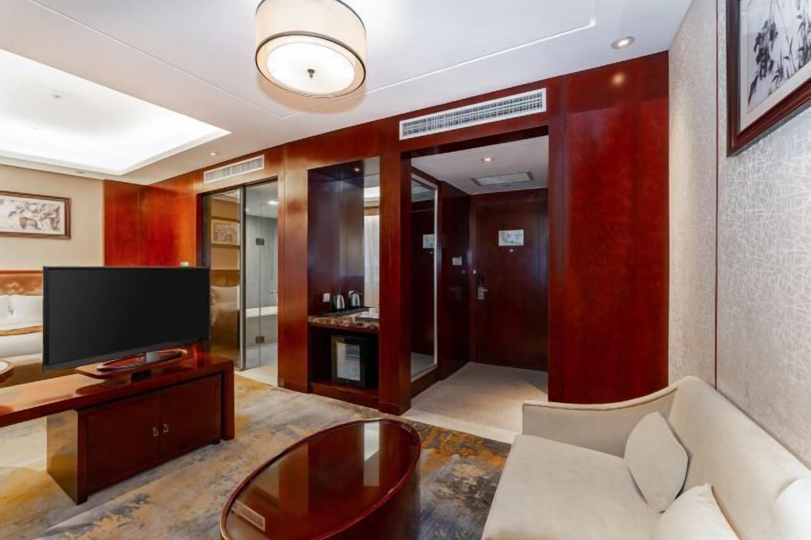 A modern hotel room with a flat-screen TV, a sofa, a coffee table, and a large window.