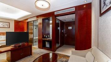 A modern hotel room with a flat-screen TV, a sofa, a coffee table, and a large window.