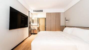 A hotel room with a bed, a TV mounted on the wall, a bedside table, a mirror, and a wardrobe.