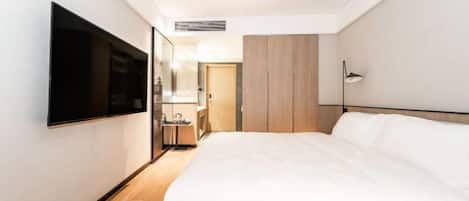 A hotel room with a bed, a TV mounted on the wall, a bedside table, a mirror, and a wardrobe.