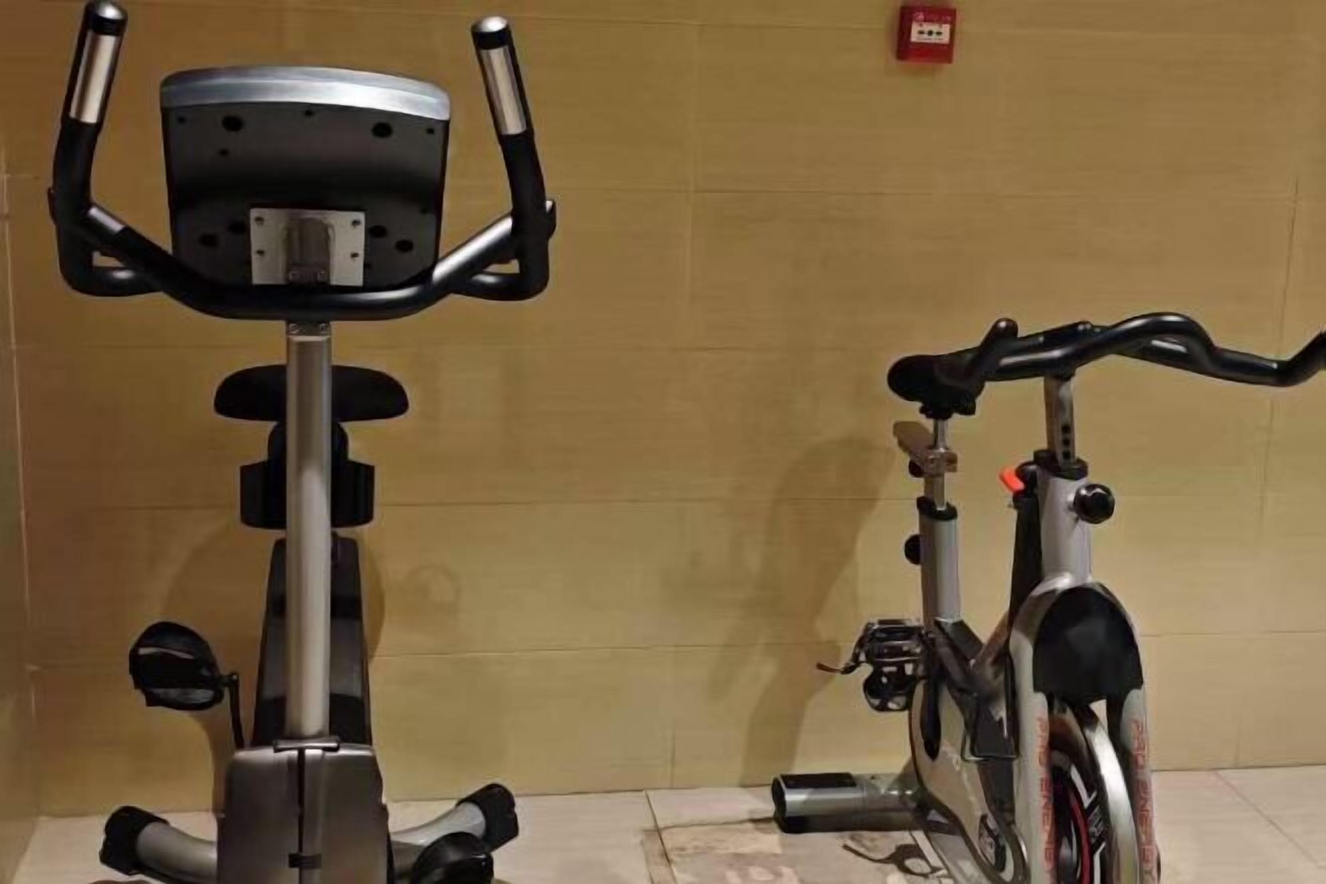 An exercise bike and a bicycle in a room with a tiled floor and a plain wall.