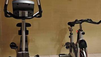 An exercise bike and a bicycle in a room with a tiled floor and a plain wall.