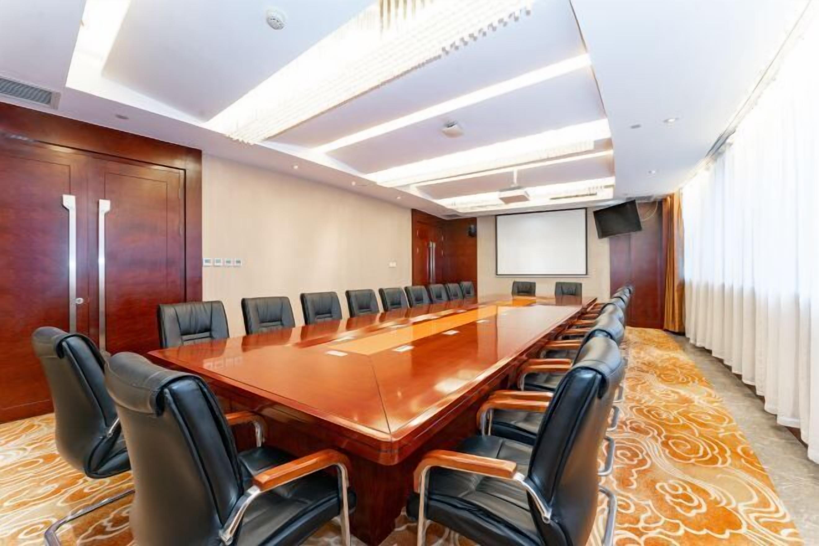 A conference room with a long table, multiple chairs, a projector screen, and a large window with curtains.