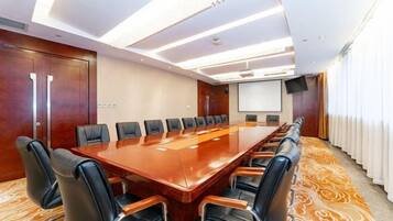 A conference room with a long table, multiple chairs, a projector screen, and a large window with curtains.